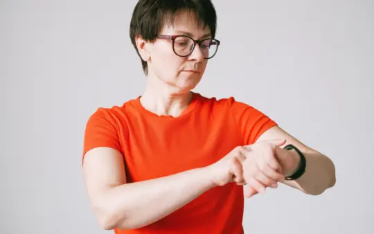 Woman in glasses checks her smartwatch in a minimalist indoor setting.