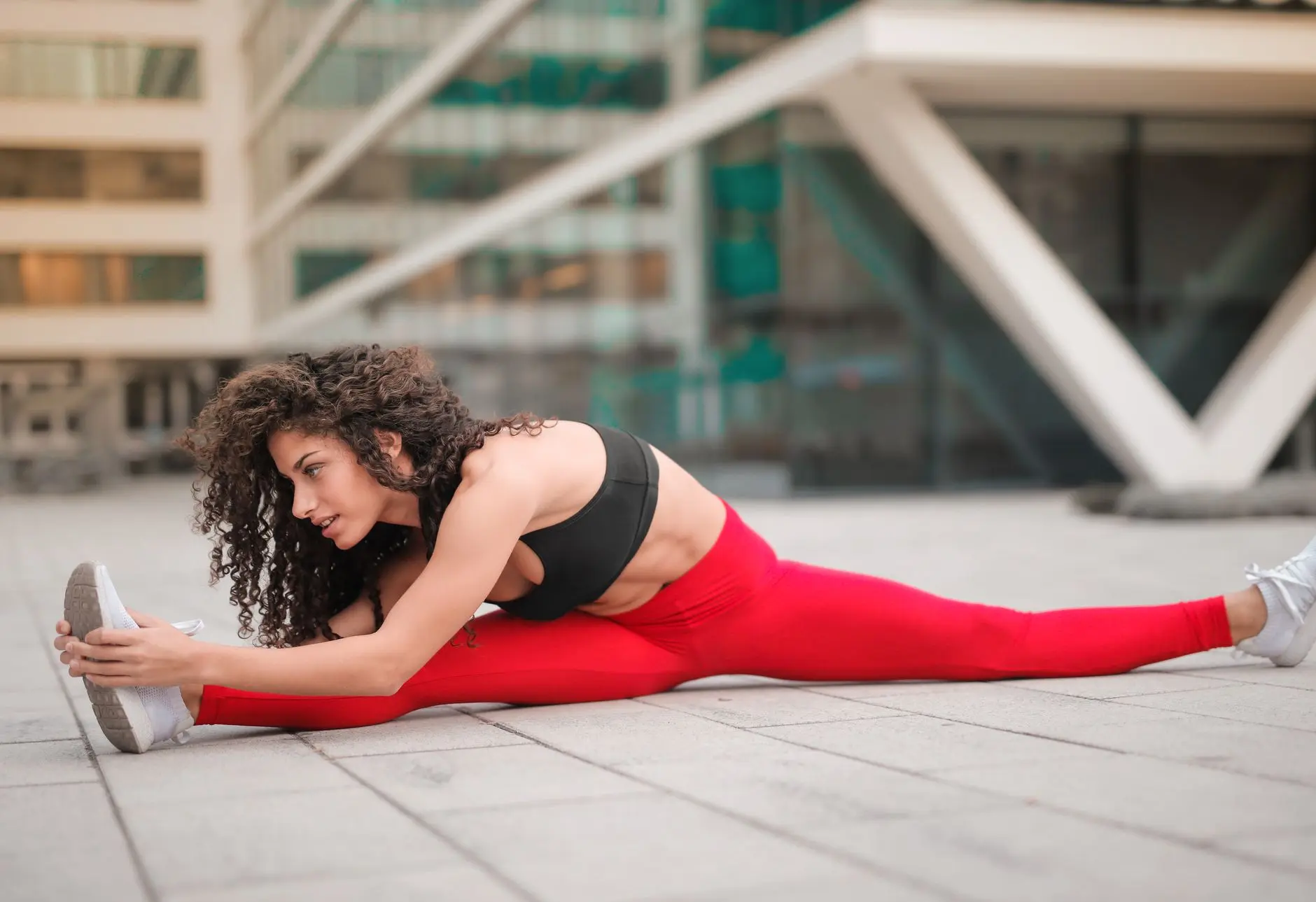A woman performs a stretching exercise in an urban environment, showcasing flexibility and fitness