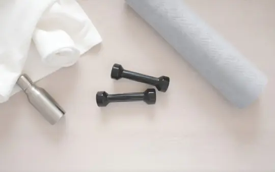 Seen from directly above, filling the frame, on a light wooden floor: a pair of small black dumbbells, a rolled white co, generated illustration