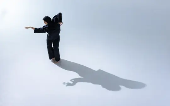 Female dancer in a hijab performs gracefully indoors, casting an artistic shadow.
