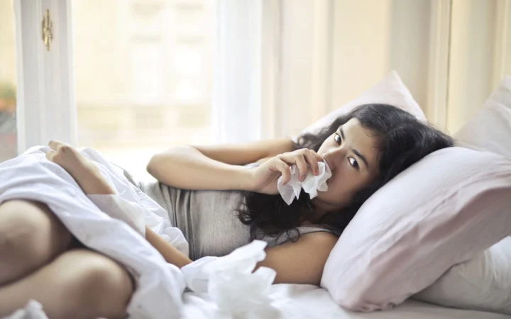 Woman lying in bed indoors, using tissue for cold and flu symptoms.