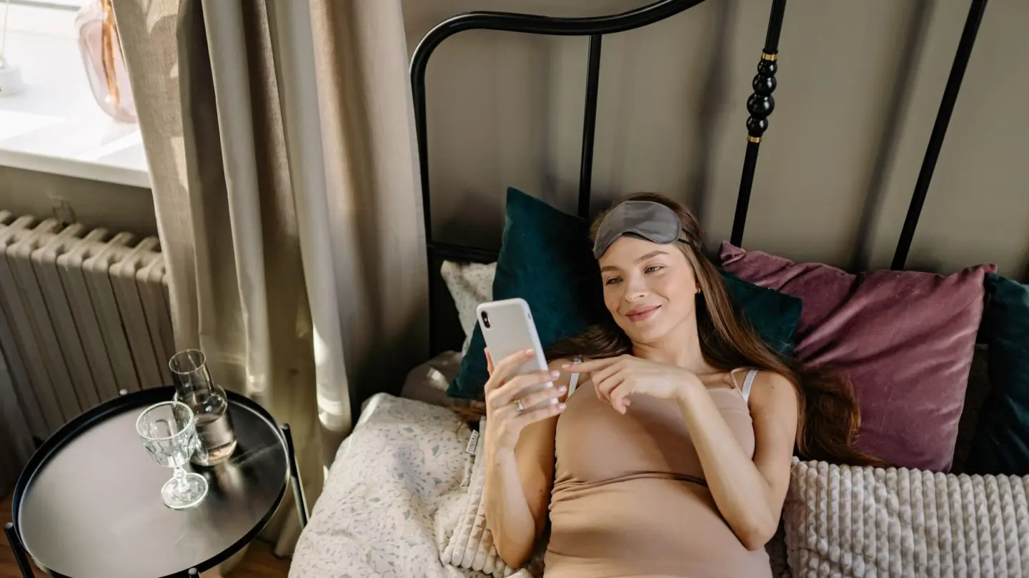 Sleep aids for pregnant women: pregnant woman lying in bed with cellphone, enjoying a relaxing morning indoors