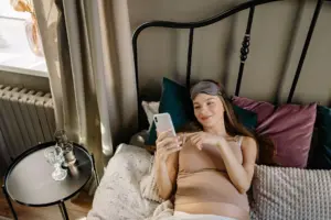 Sleep aids for pregnant women: pregnant woman lying in bed with cellphone, enjoying a relaxing morning indoors