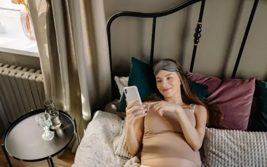 Sleep aids for pregnant women: pregnant woman lying in bed with cellphone, enjoying a relaxing morning indoors