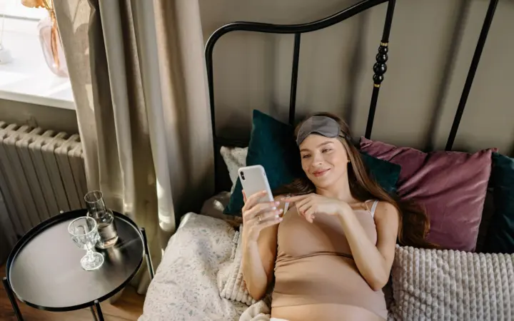 Sleep aids for pregnant women: pregnant woman lying in bed with cellphone, enjoying a relaxing morning indoors