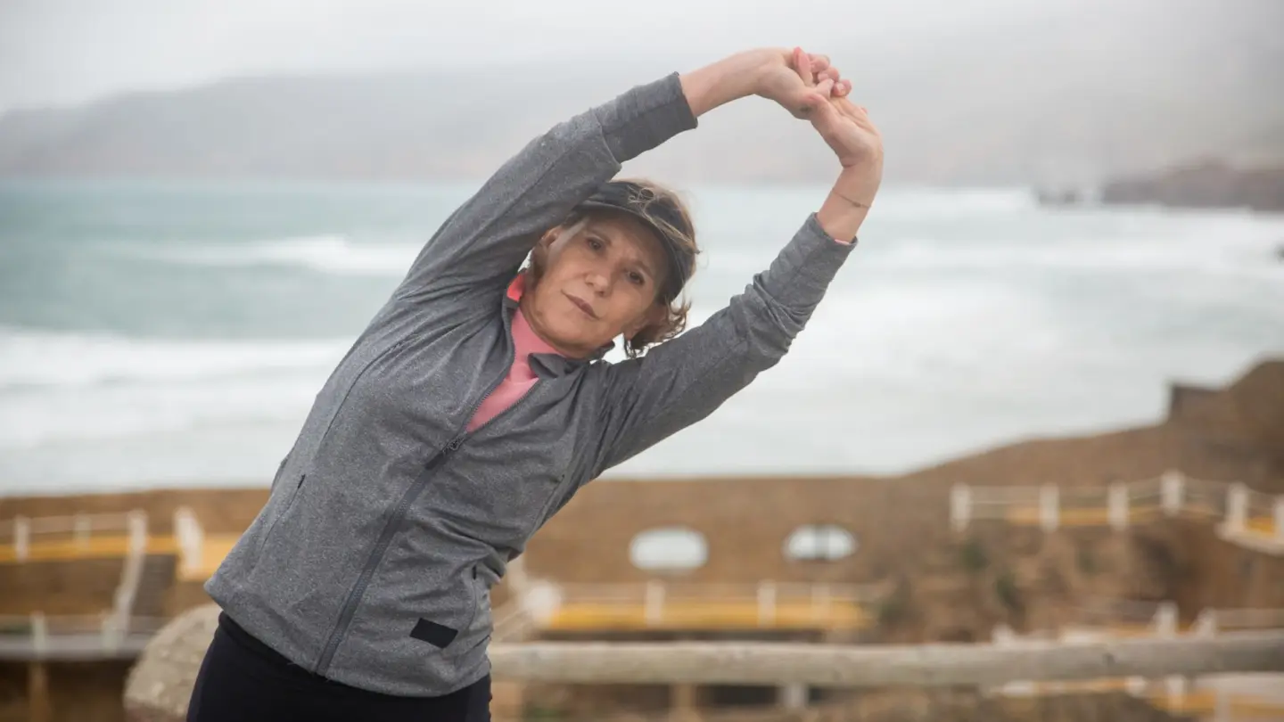 Strength training routines for women over 50: senior woman stretching outdoors by the seaside in Portugal, embracing a