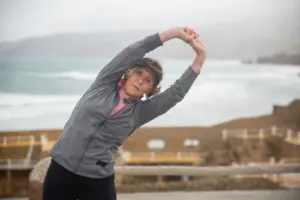 Strength training routines for women over 50: senior woman stretching outdoors by the seaside in Portugal, embracing a