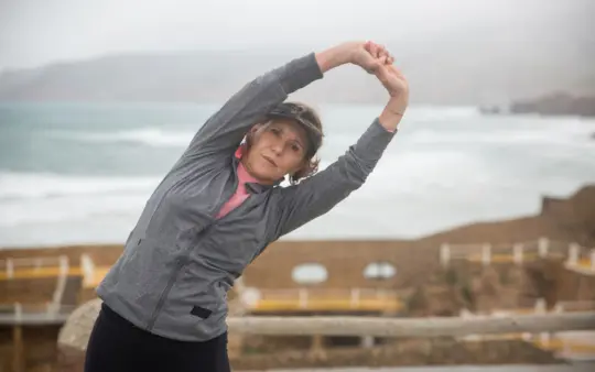 Strength training routines for women over 50: senior woman stretching outdoors by the seaside in Portugal, embracing a