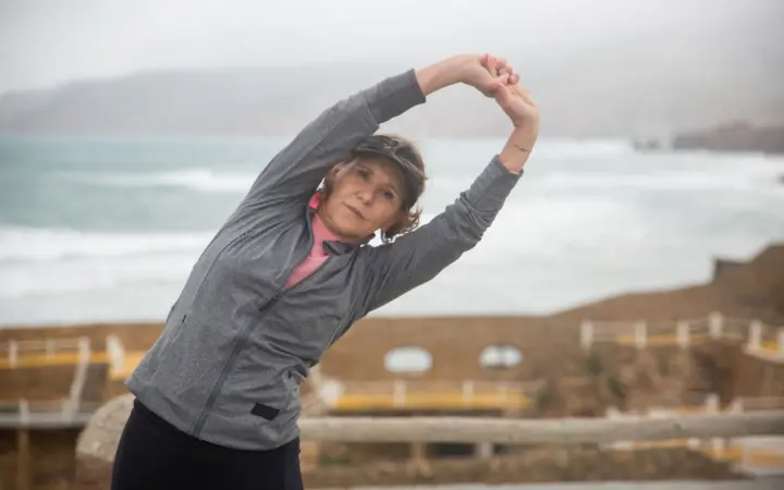 Strength training routines for women over 50: senior woman stretching outdoors by the seaside in Portugal, embracing a