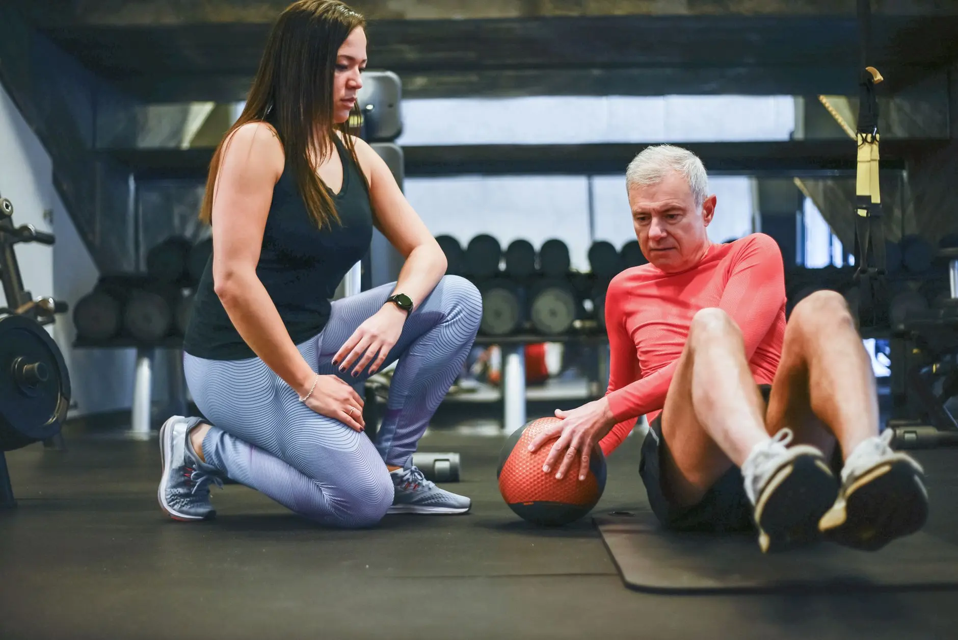 A senior man exercising with a personal trainer in a gym, focusing on core workouts
