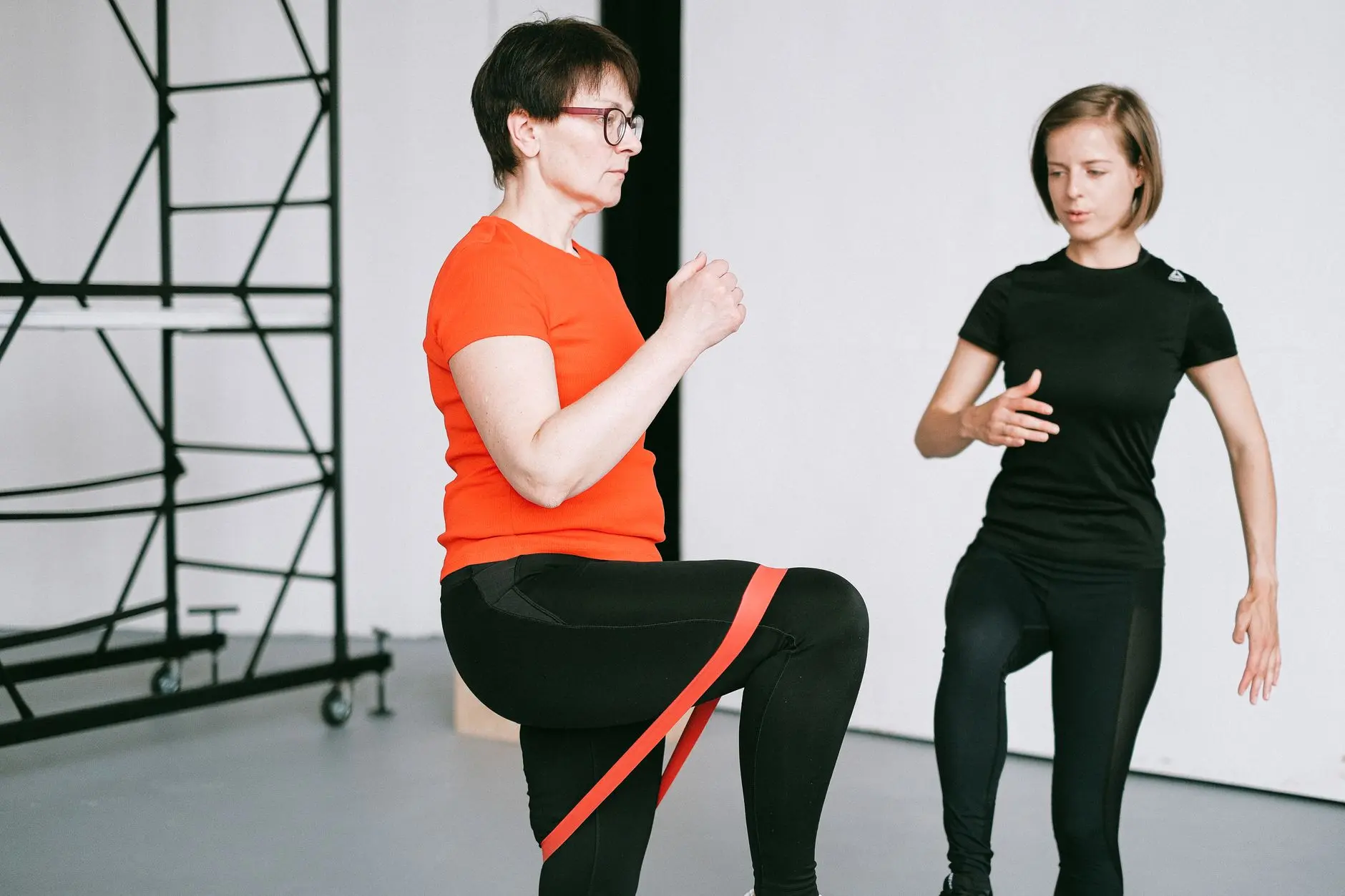 Personal trainer guiding a woman with resistance band exercise in a gym setting