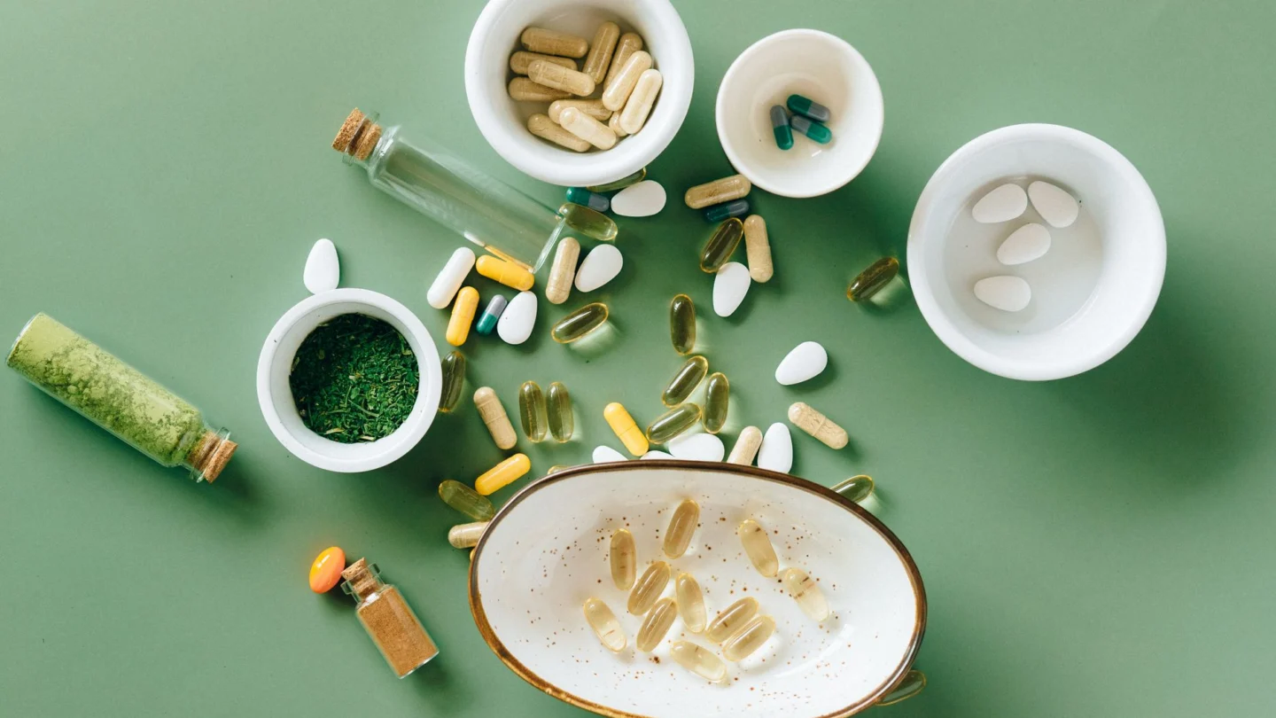 Top view of various herbal and pharmaceutical supplements in ceramic bowls on a green background.