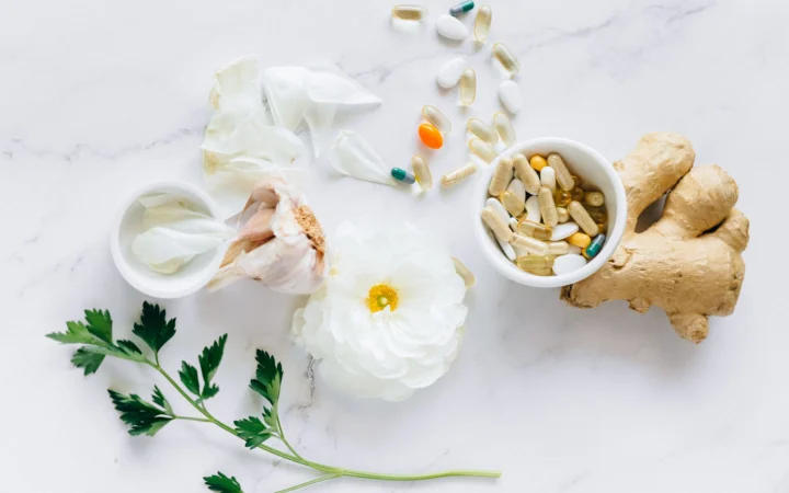 Top view of herbal medicine and supplements with ginger, flower, and capsules on a white background.
