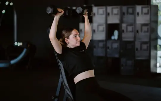 Young woman lifting dumbbells at gym showcasing strength training and fitness lifestyle.