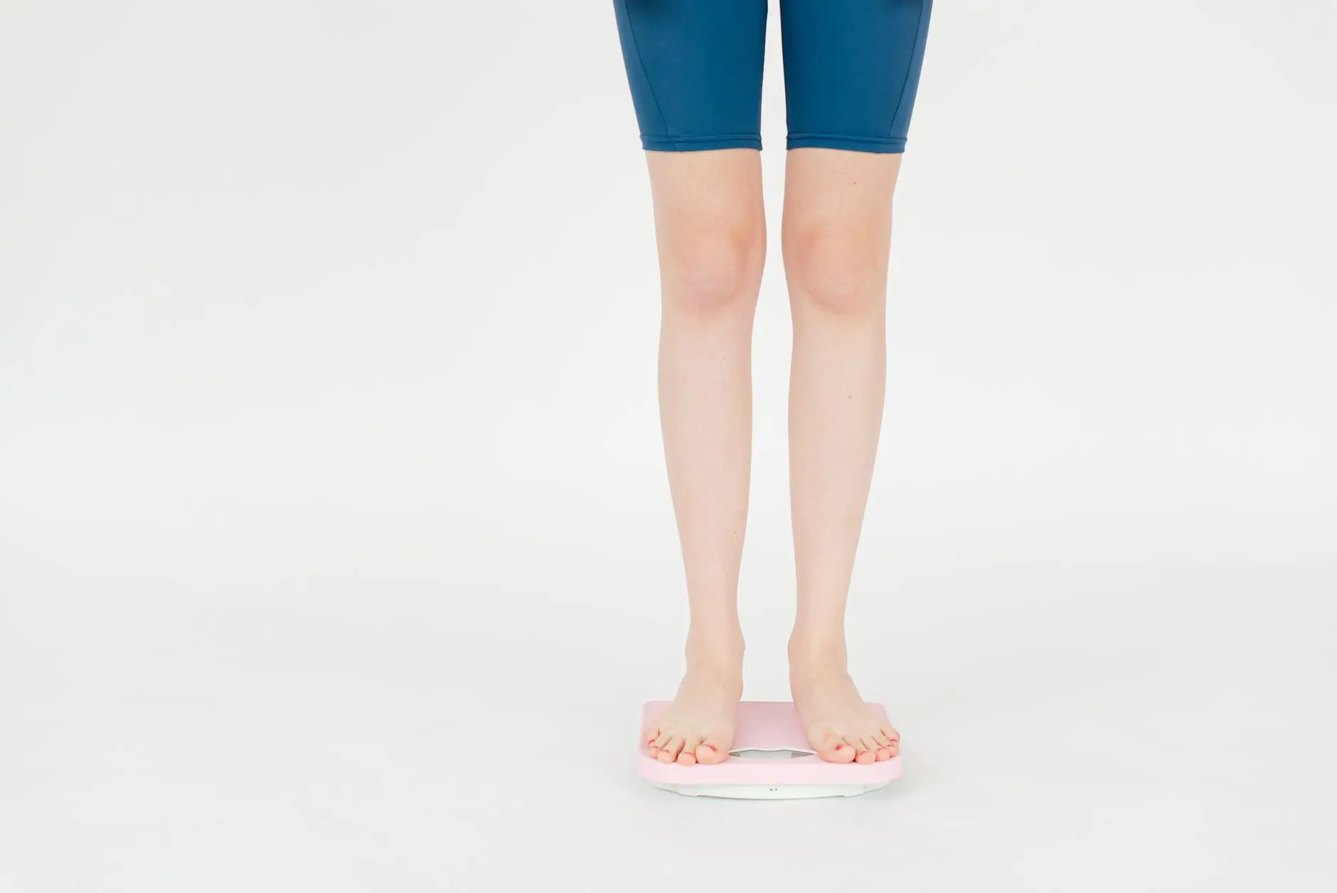 Crop anonymous female in sportswear measuring weight on scales for body control against white background