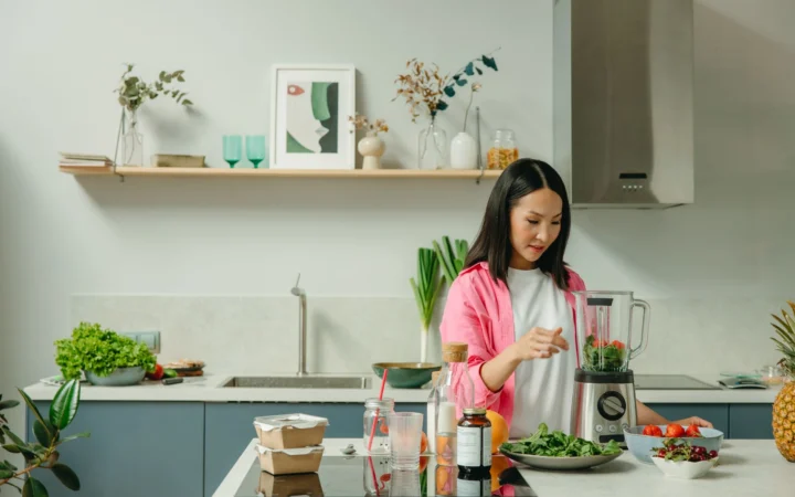 Asian woman blending fresh fruits and vegetables in a stylish kitchen setting.