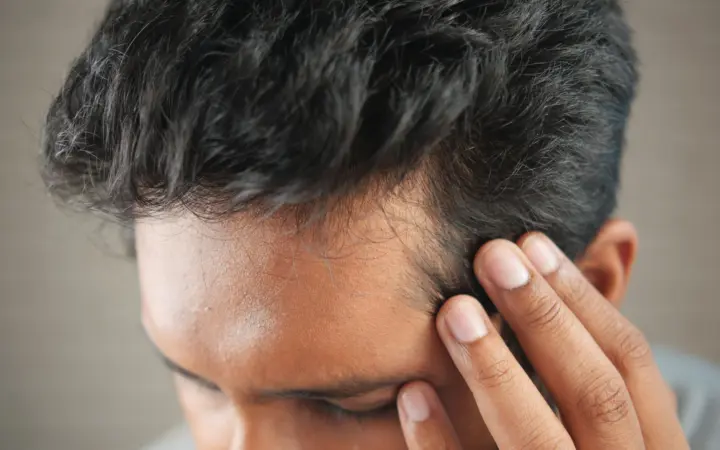 Can vitamin d deficiency cause hair thinning: close-up of a man's hand touching his head in contemplation