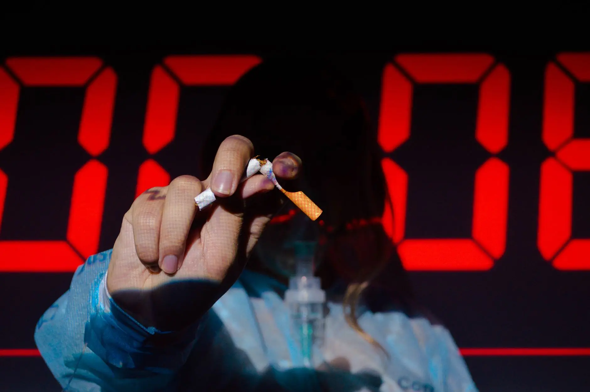 A hand holding a broken cigarette in front of a digital timer, highlighting the urgency of quitting smoking