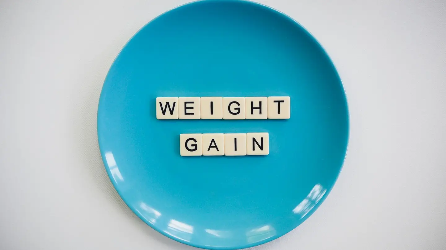 Does low progesterone cause weight gain: scrabble tiles spelling 'weight gain' on a blue plate, symbolizing health and diet