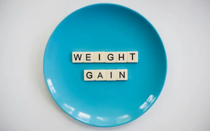 Does low progesterone cause weight gain: scrabble tiles spelling 'weight gain' on a blue plate, symbolizing health and diet