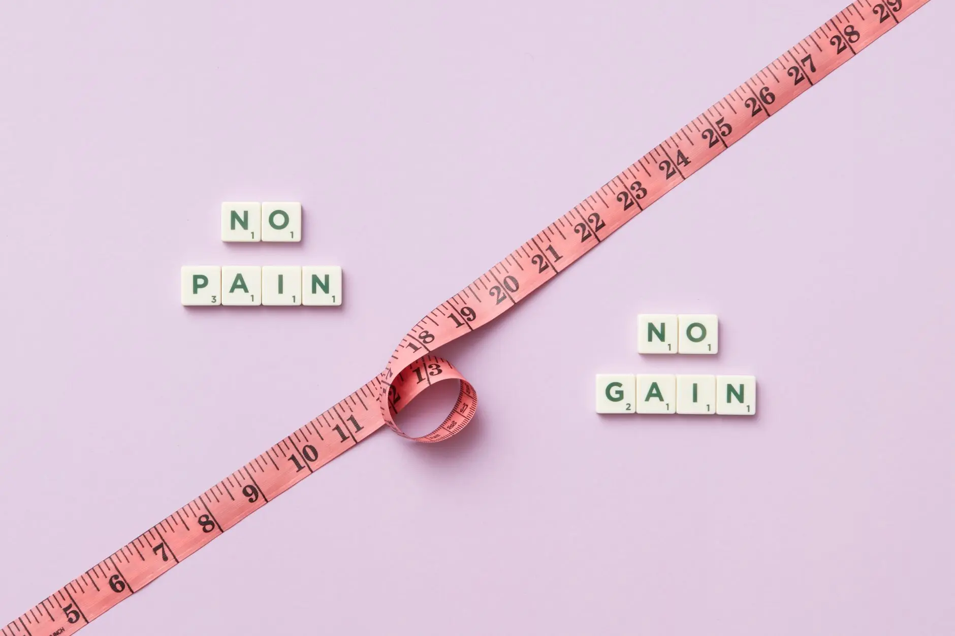 Pink tape measure with 'No Pain No Gain' spelled in Scrabble tiles on pink background