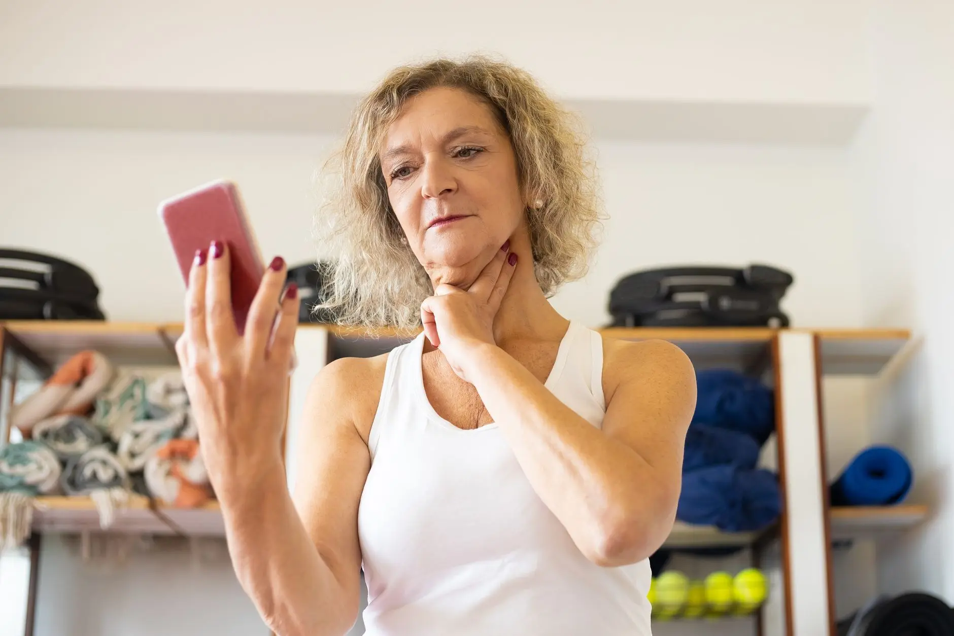 Middle-aged woman checking pulse on smartphone during fitness routine indoors
