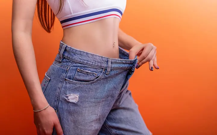 How long can weight loss plateau last: a woman holding loose jeans against her slim waist, symbolizing successful weight loss
