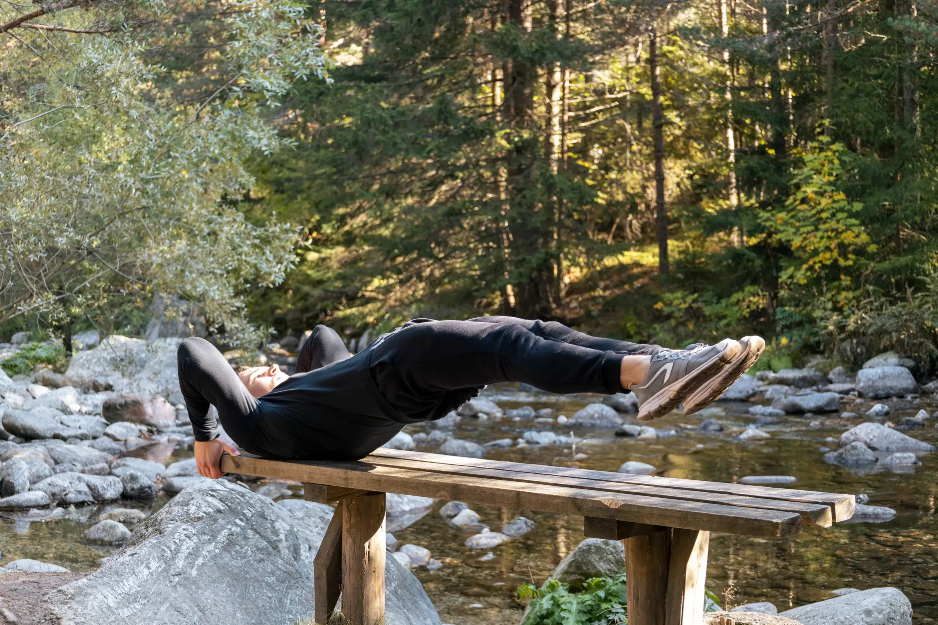 Man performing a core exercise on a bench by a serene river in a forest setting