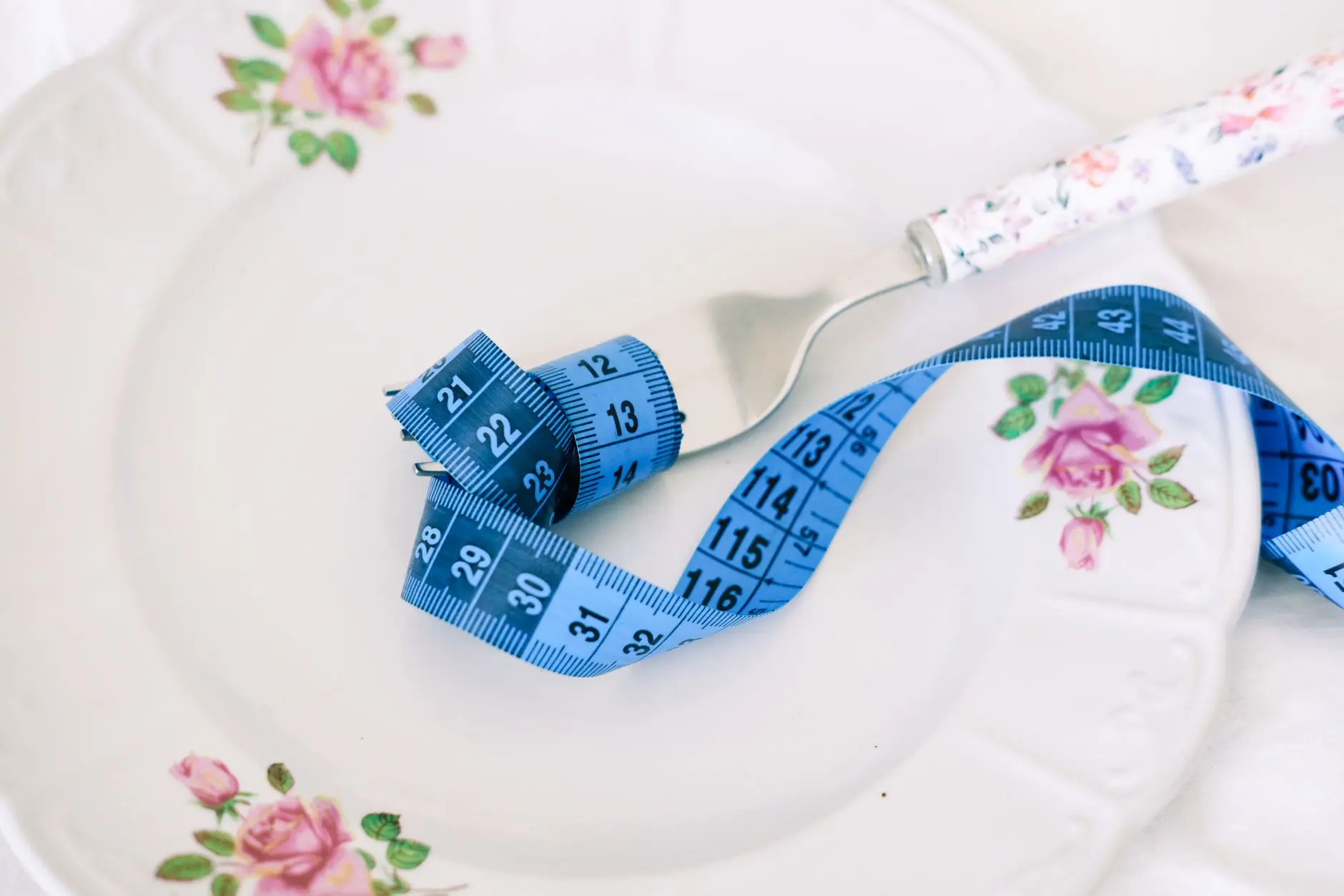 A floral plate with a fork and blue measuring tape symbolizing dieting or healthy eating