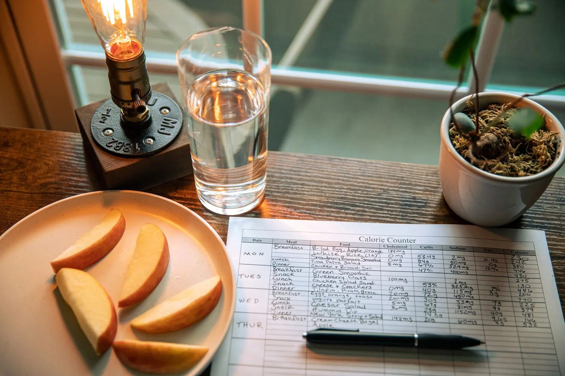 A cozy desk setup with apple slices, calorie counter, and water glass in warm lighting