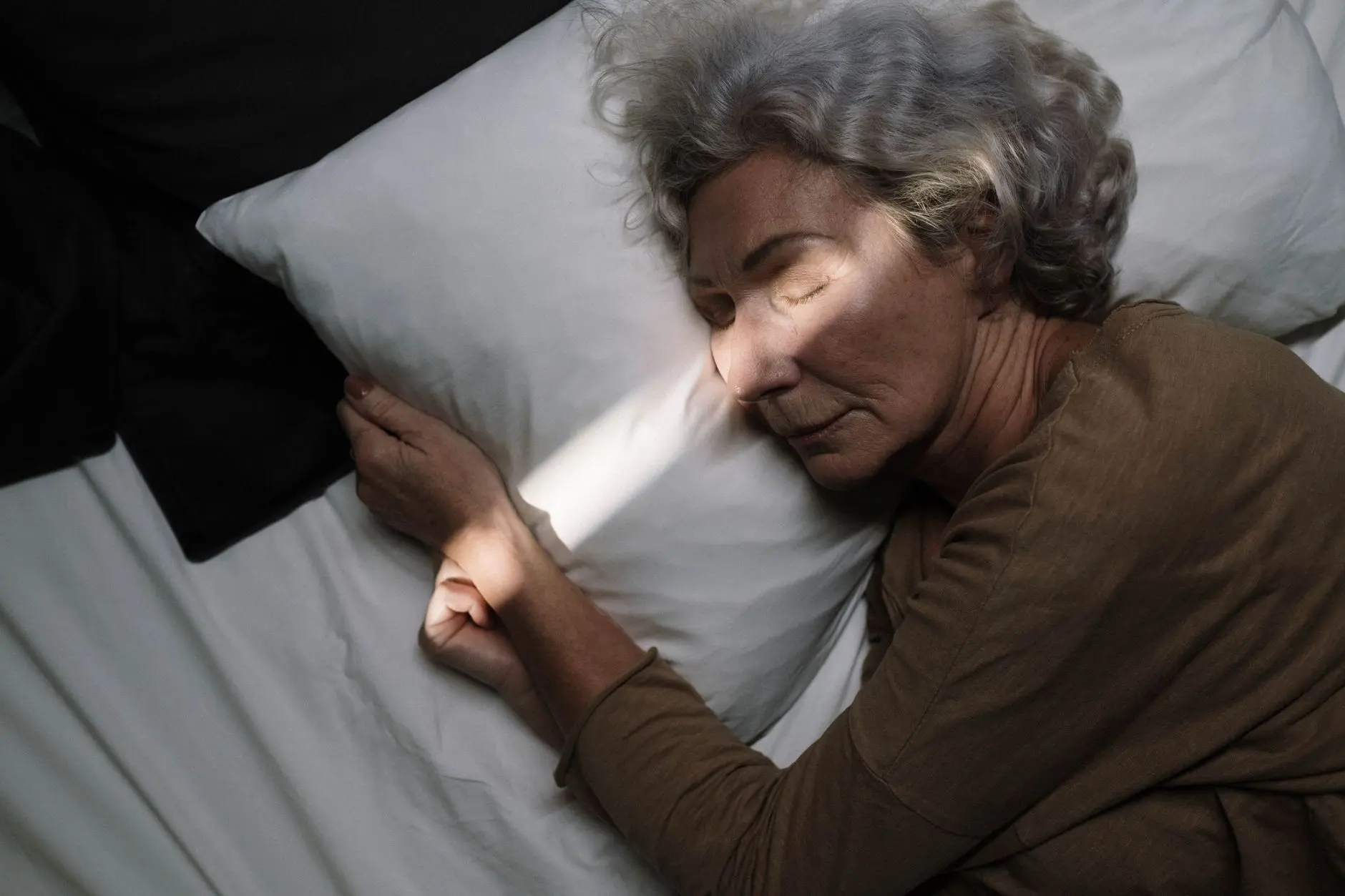 A serene moment of an elderly woman peacefully sleeping on a bed with soft lighting