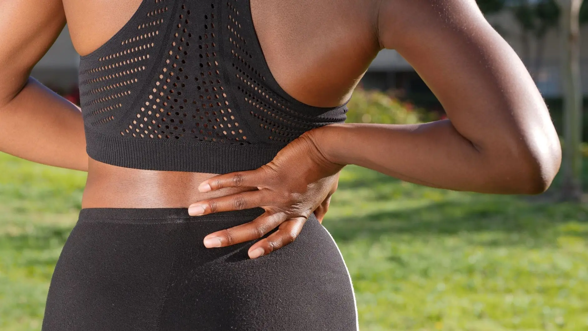 Woman in athletic attire holding her back outside, indicating discomfort or pain