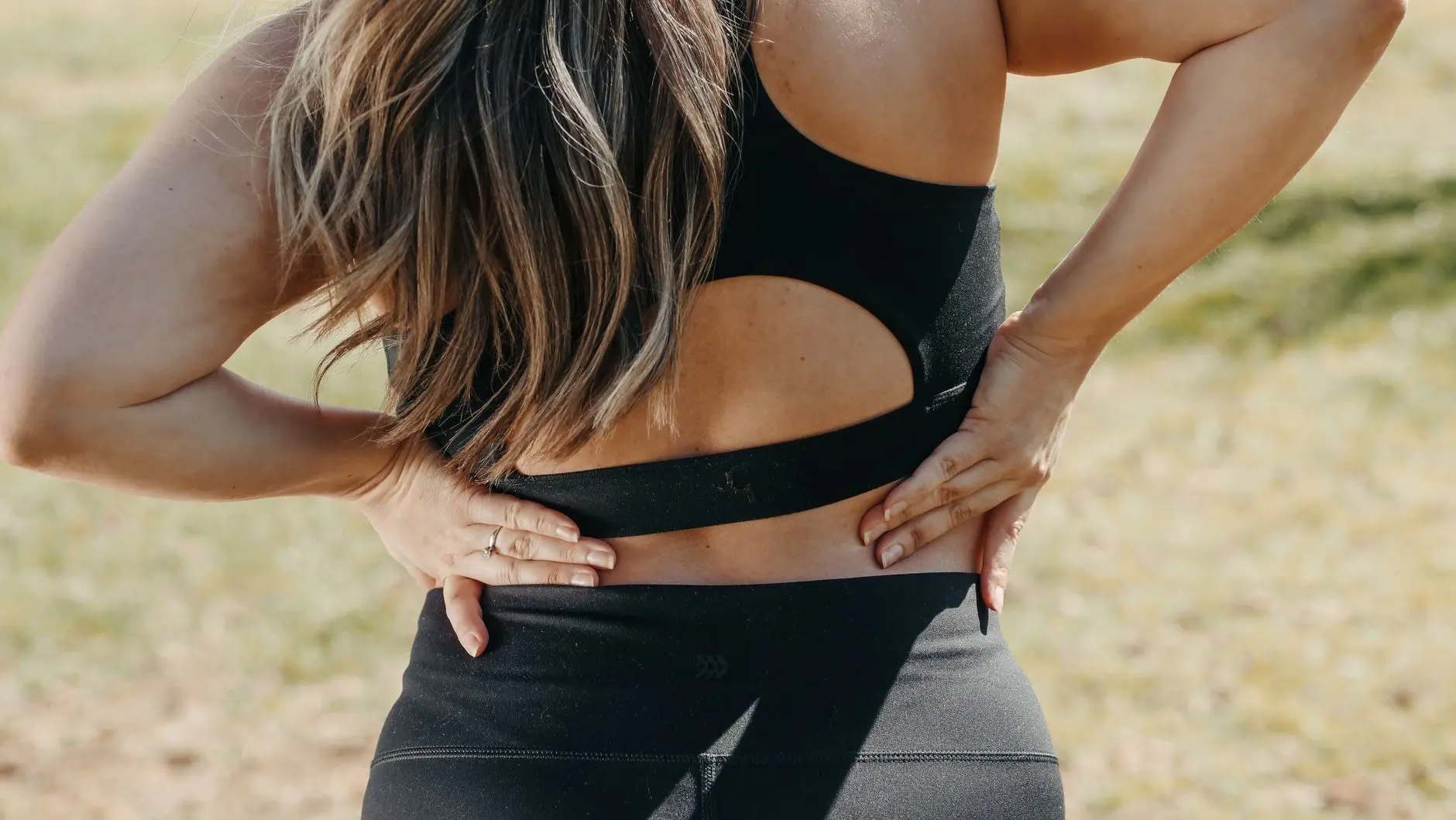 Close-up of a woman holding her back, suggesting back pain outdoors