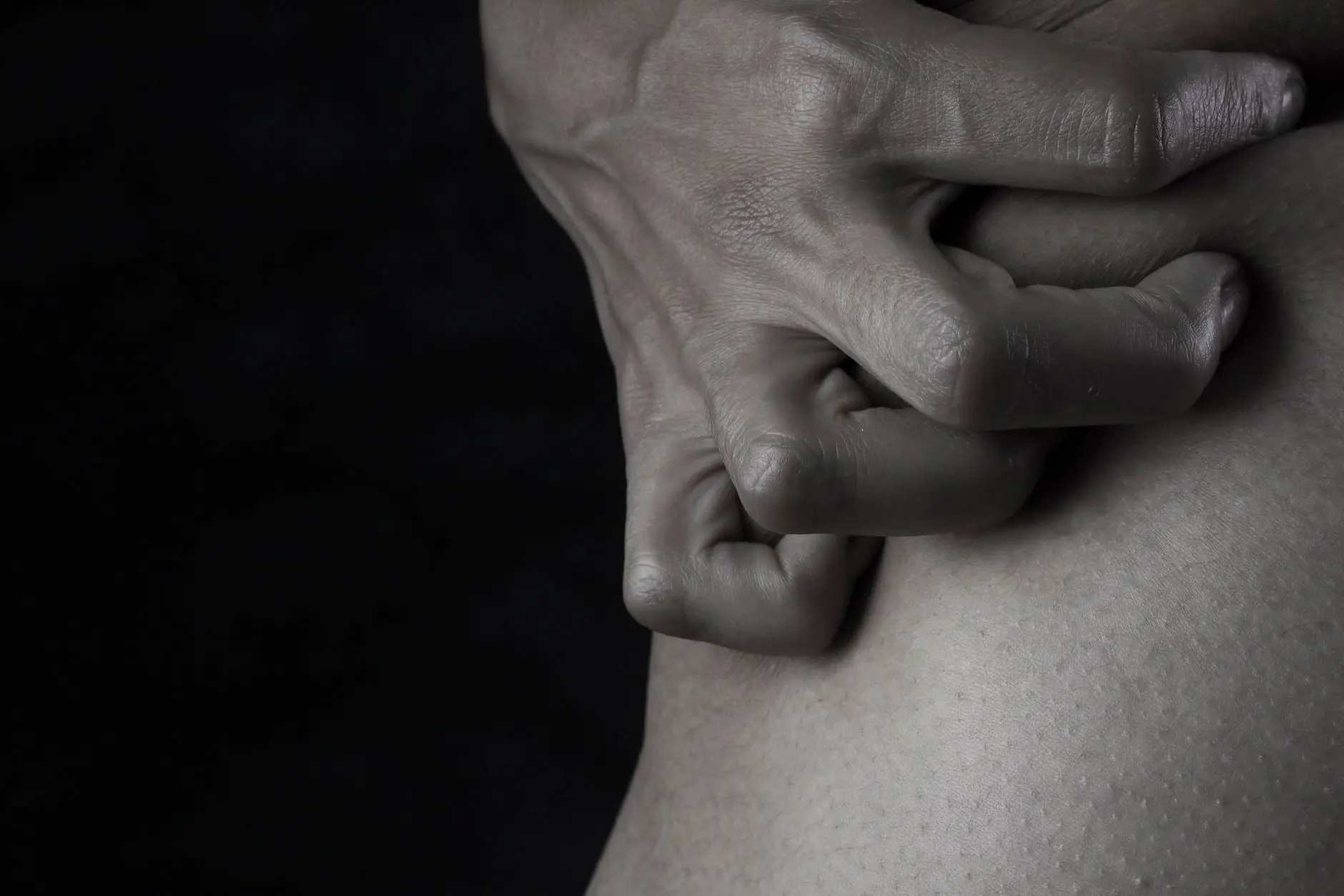 Close-up of a hand gripping skin, emphasizing emotion and tension with a dark, moody backdrop