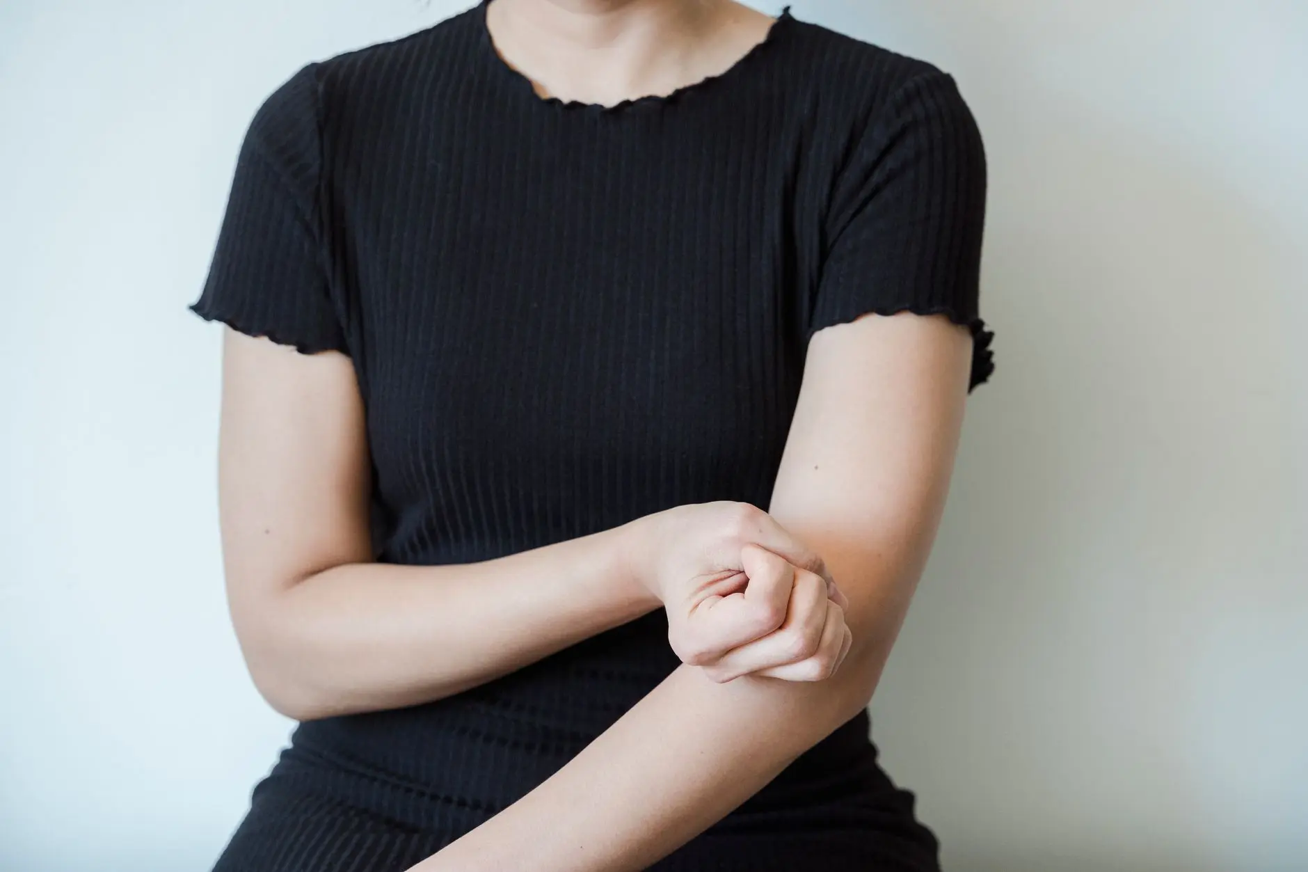 A close-up view of a woman in a black shirt holding her arm, showcasing skin contact and emotion
