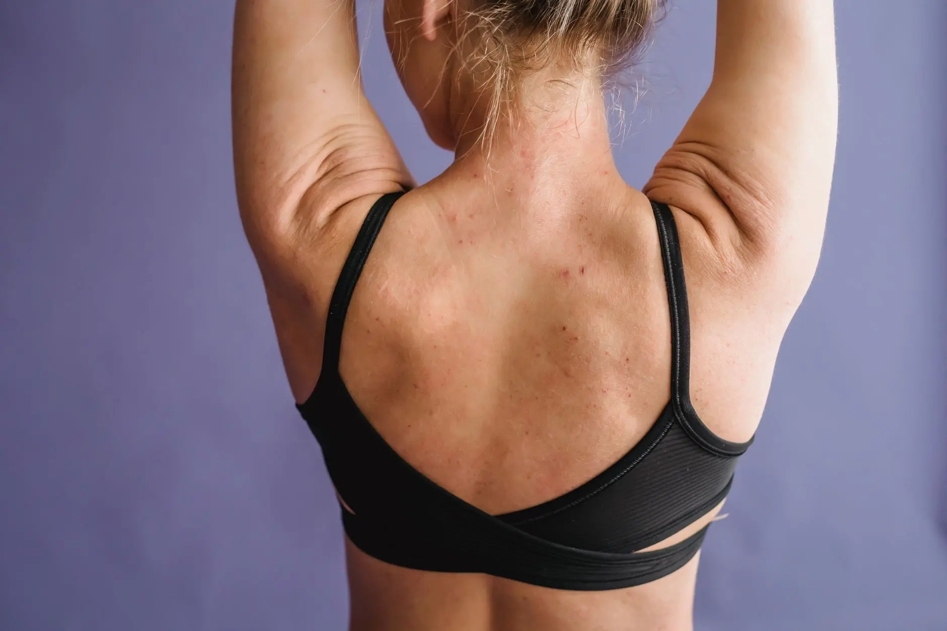 Back view of crop anonymous female with muscular arms on purple background of studio