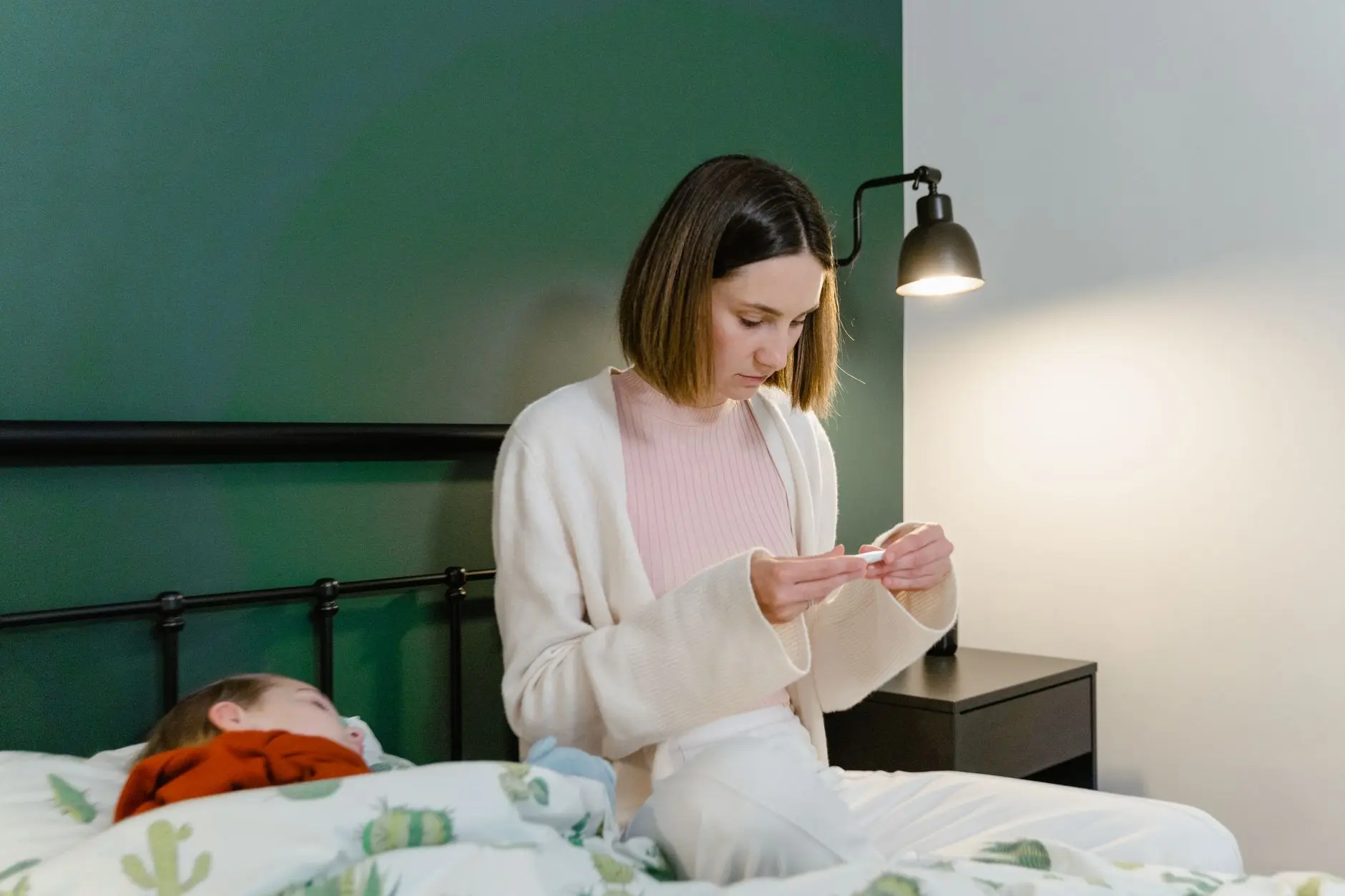 A concerned mother checks her sick child's temperature in a bedroom setting