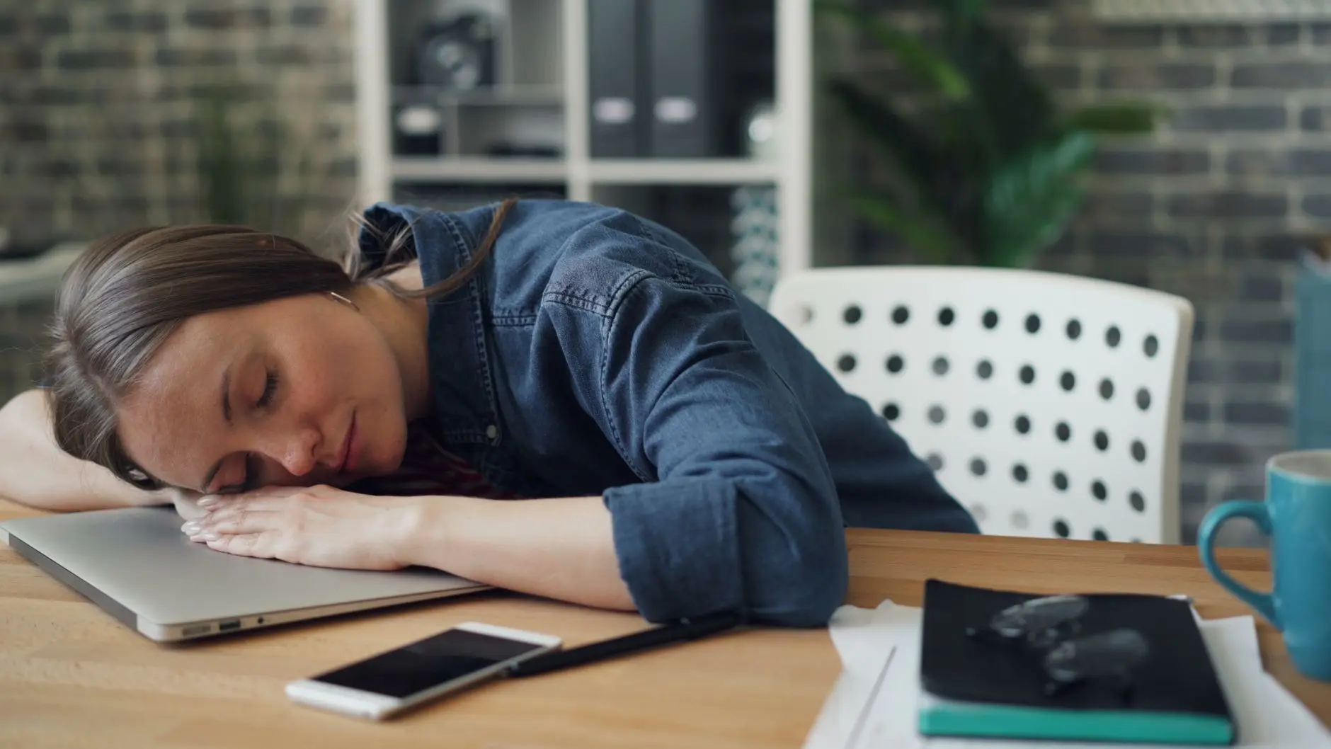 Tired woman resting her head on a laptop at an office desk, symbolizing workplace fatigue