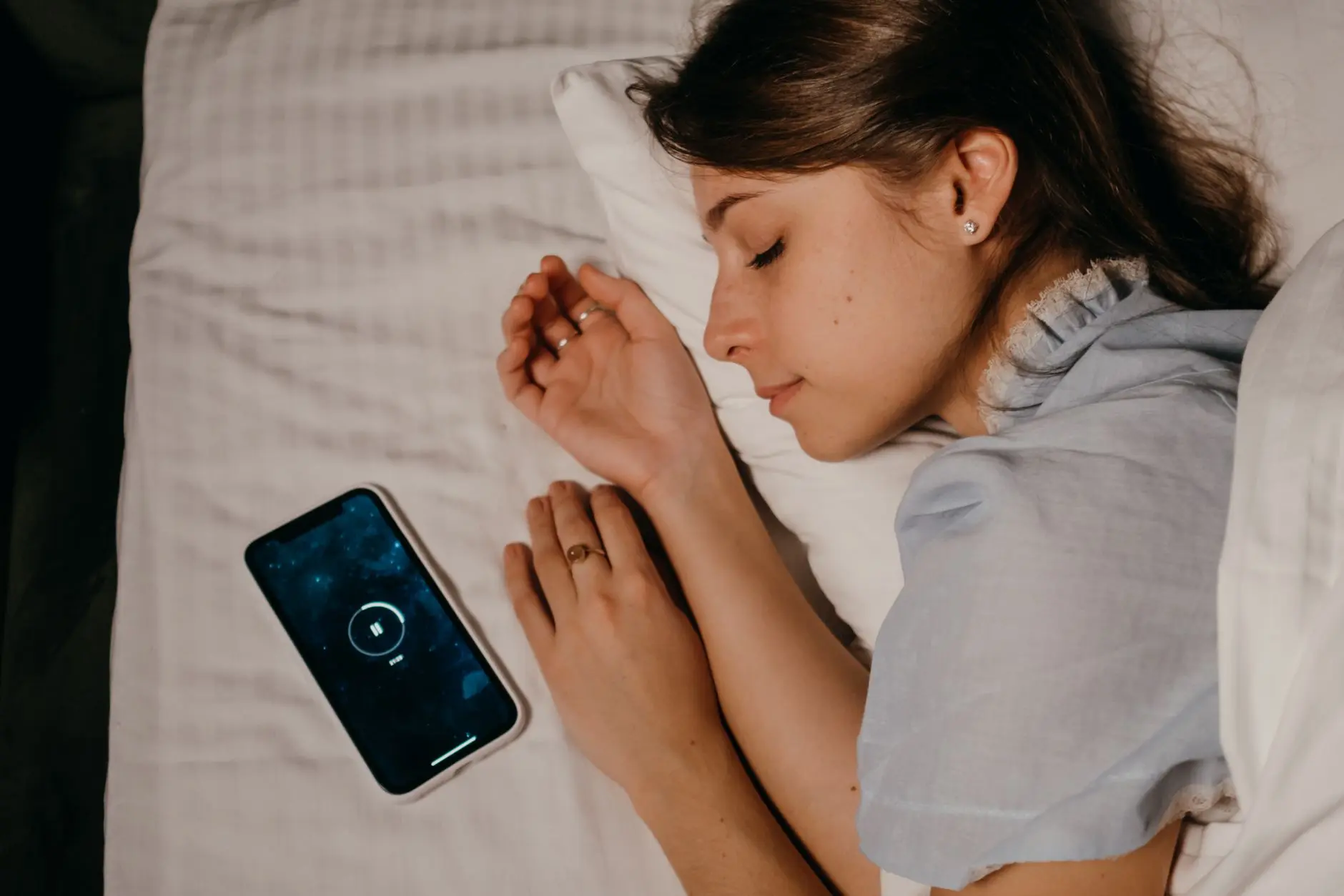 A woman peacefully sleeps in bed with a smartphone beside her, illustrating modern bedtime habits