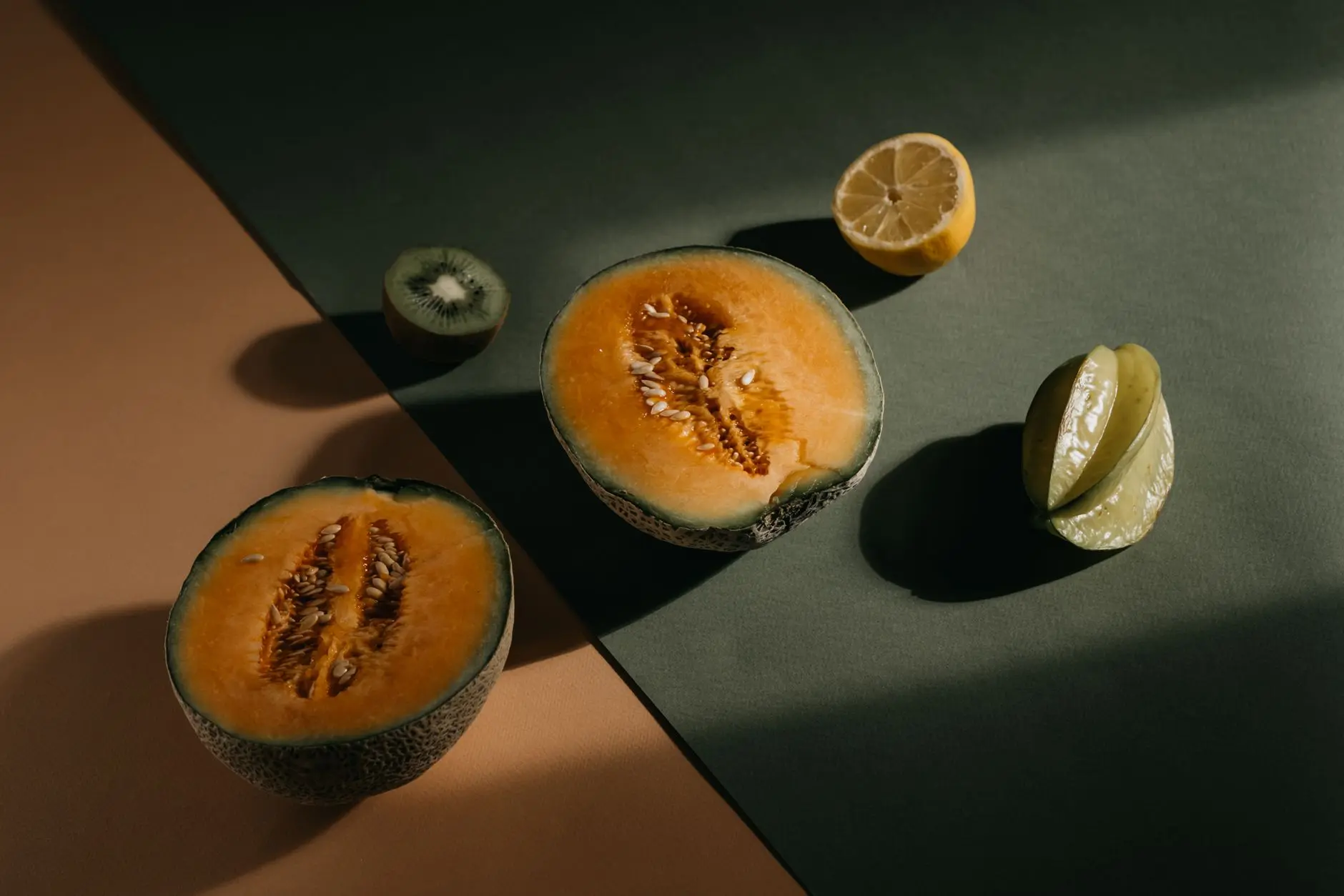 A visually appealing flat lay of fresh fruits including cantaloupe, kiwi, lemon, and starfruit on a two-toned background