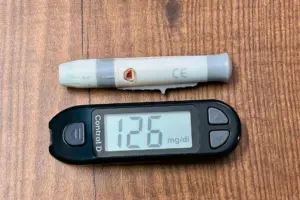 Vitamin d deficiency in blood test: a digital glucometer displaying 126 mg/dL with a lancing device placed on a wooden