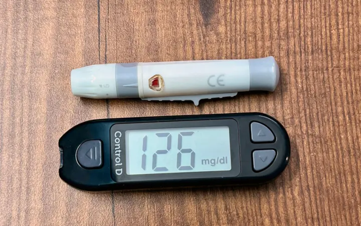 Vitamin d deficiency in blood test: a digital glucometer displaying 126 mg/dL with a lancing device placed on a wooden