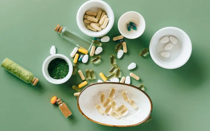 Vitamin supplements for perimenopause: top view of various herbal and pharmaceutical supplements in ceramic bowls on a green