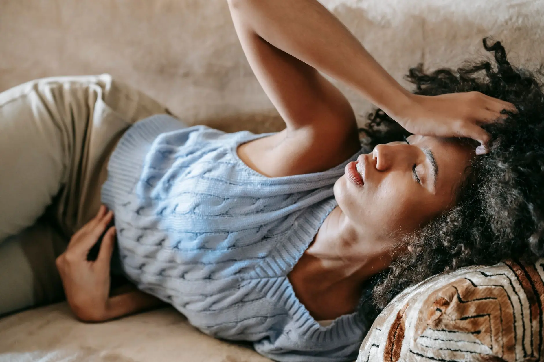 Young African American female lying on couch and touching forehead while having headache
