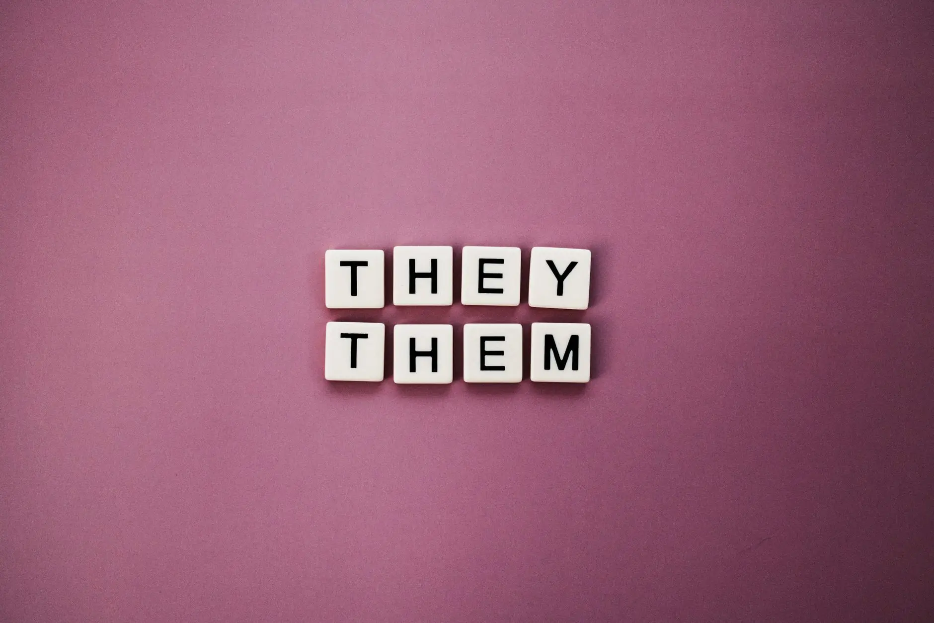 Non-binary pronouns 'they them' displayed with letter tiles on a pink backdrop