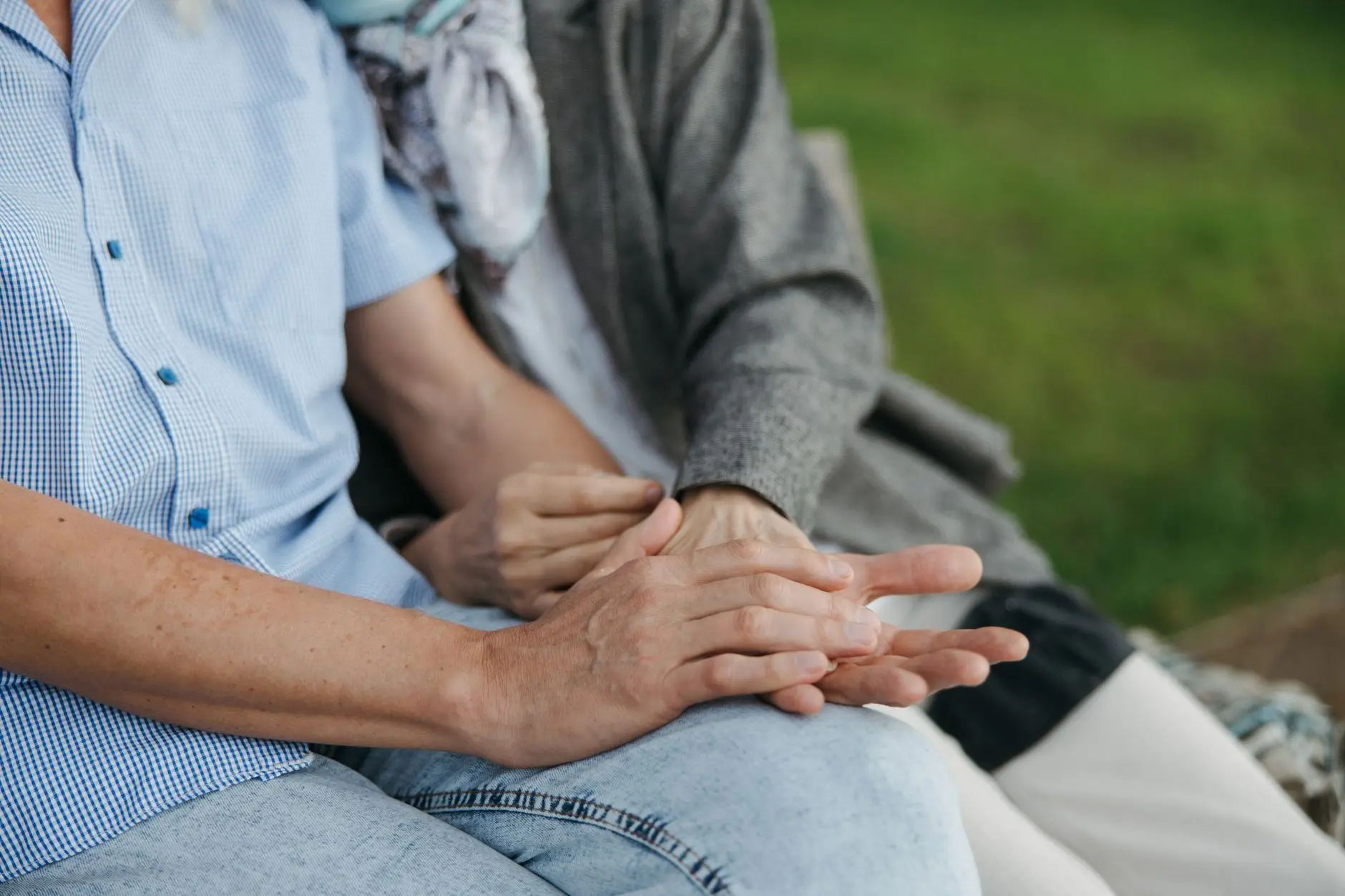 Close-up of elderly couple holding hands on a bench, symbolizing love and companionship