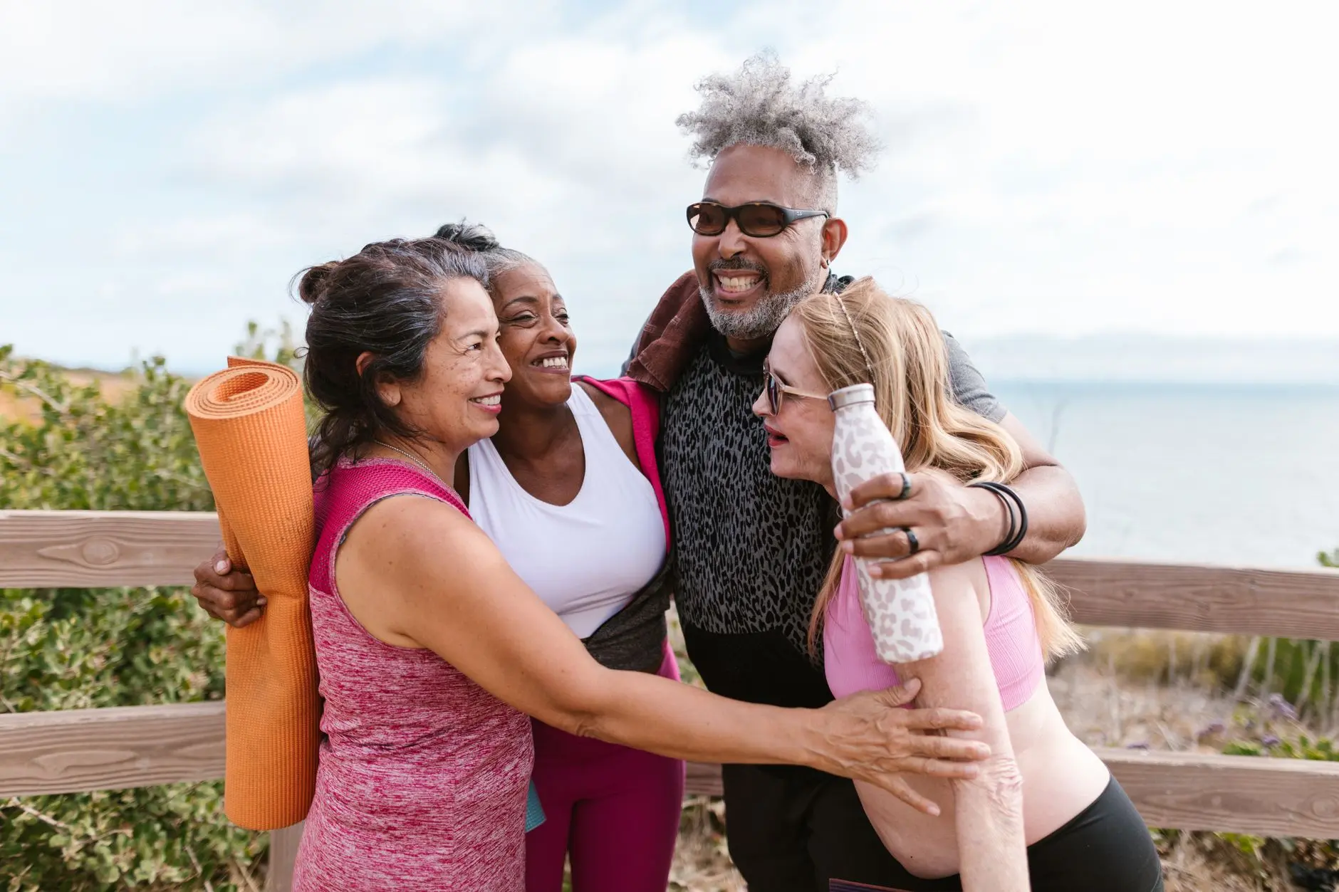 Happy senior friends embracing after a yoga session by the beach, enjoying the outdoors together