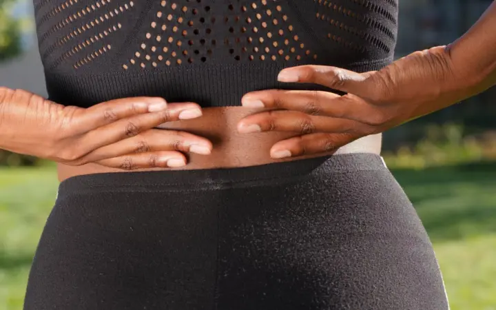 What is the cause of lower back pain in women: close-up of a woman's hands gripping her painful back while outdoors