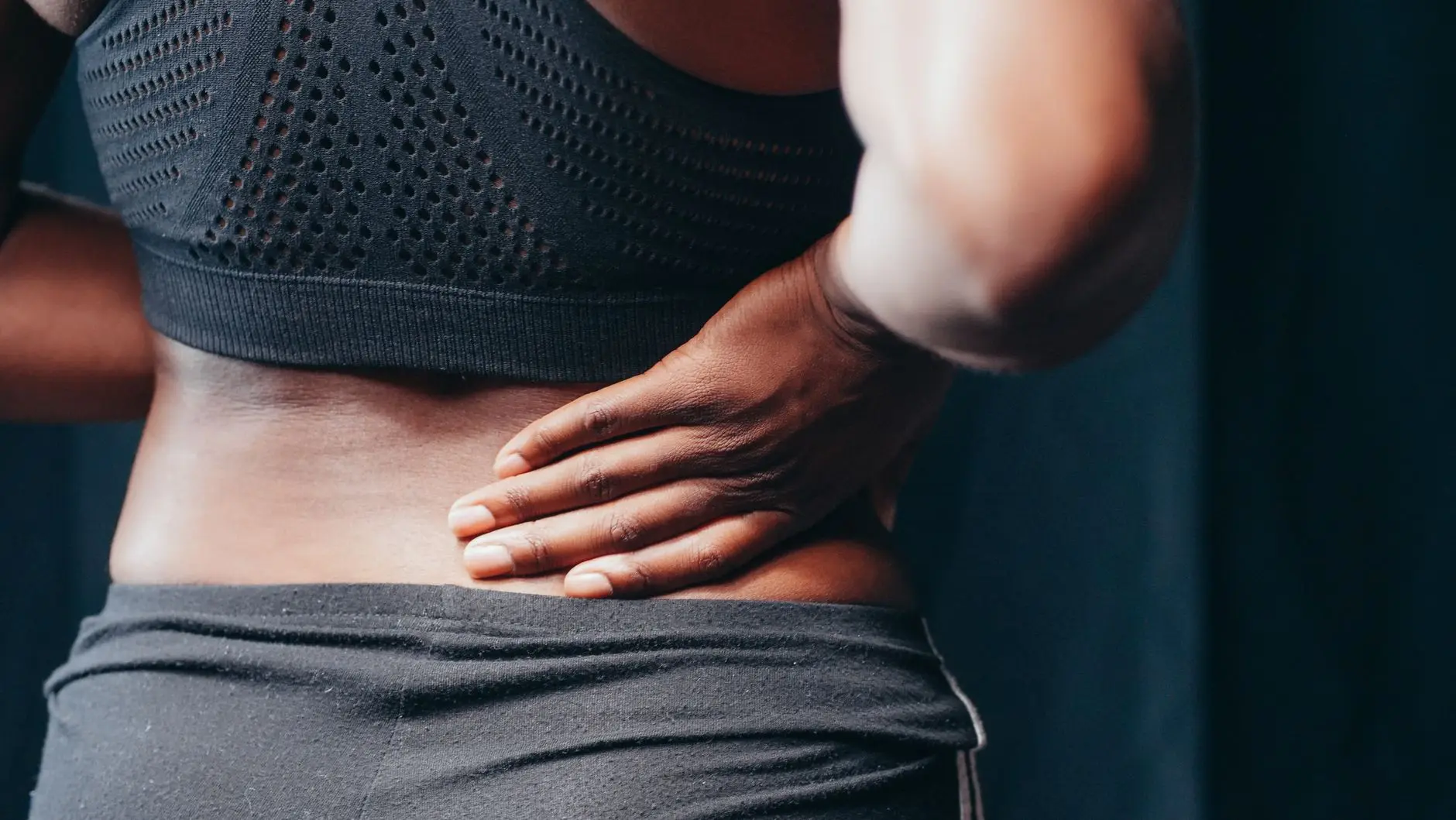An adult of African descent holding their lower back in pain, indicating discomfort or injury