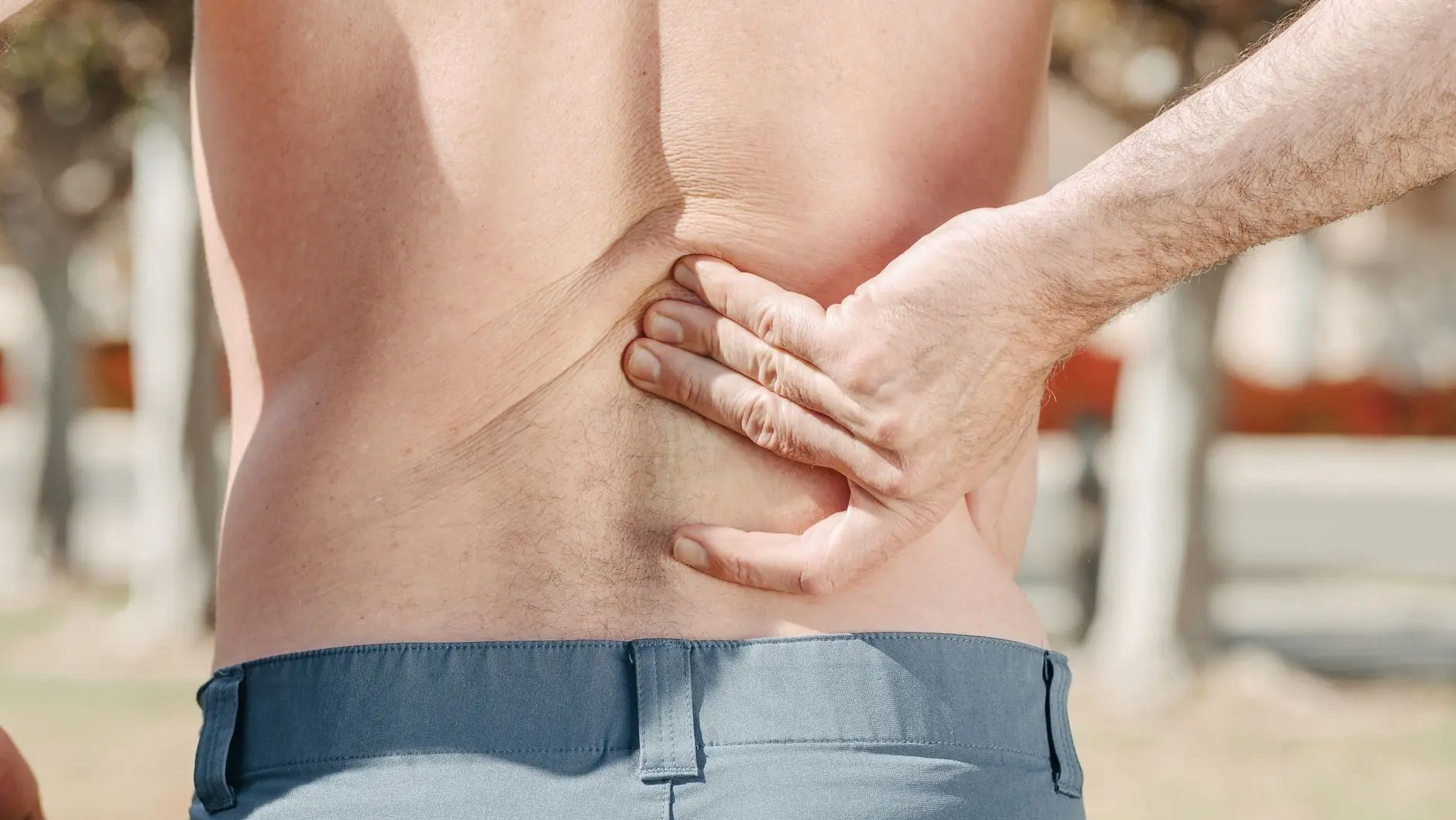 Close-up of a man holding his lower back in pain, possibly indicating discomfort or injury